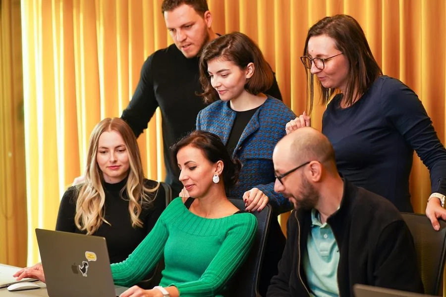 Employees gathered around a laptop, collaborating and optimizing knowledge management solutions to improve communication and workflow